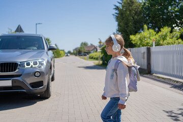 Girl with headphones and cellphone crossing the road, not looking at car let