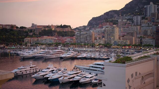 Cityscape of Monaco at sunset. Sea port with moored yachts, residential buildings and streets with illumination
