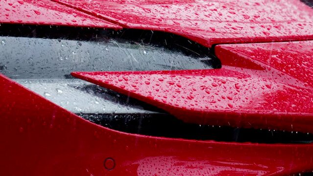 View of the front lights of a parked red supercar in the rain. Slow motion
