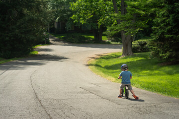 Young boy riding blue balance bike on suburban street.