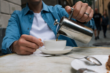 man pouring coffee into a cup at a cafe in the city - obrazy, fototapety, plakaty