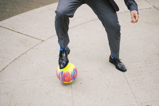 Man in suit plays kickball, action shot.