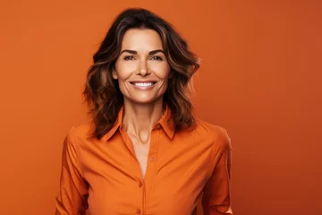 Fotobehang 40 - year - old woman wearing a bright clothes next to a orange background. Beautiful businesswoman, who is smiling and laughing at isolated background. © radekcho