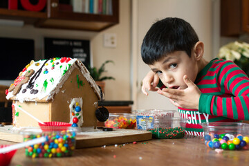 Young boy sneaking candy while decorating a gingerbread house.