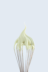 Whisk with whipped cream on gray background close up.