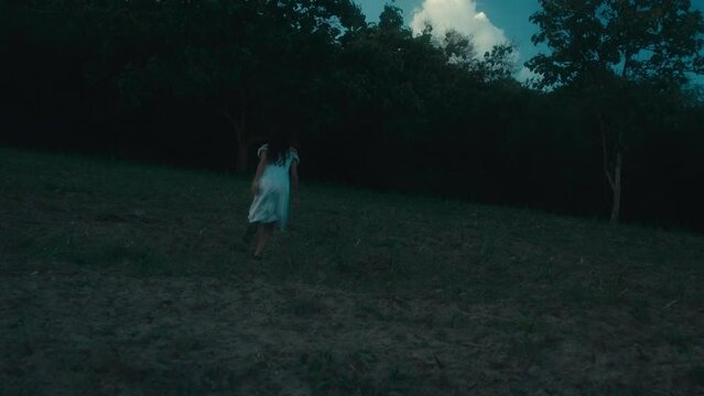 A frightened girl in a bloodstained dress runs away from her pursuer through the woods