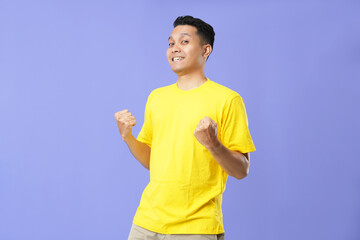 Photo of a happy young Asian man raising his fists doing a yes gesture, isolated on a soft blue...