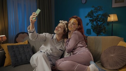 Portrait of young couple spending time together. Man and woman sitting on the sofa, wearing face masks, taking selfie on smartphone.