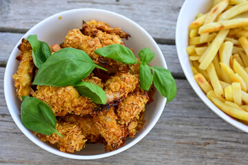  Crispy home made  deep fried   chicken strips . Breaded  with cornflakes chicken  breast fillets  with chilly peppers and fresh   basil on wooden rustic background