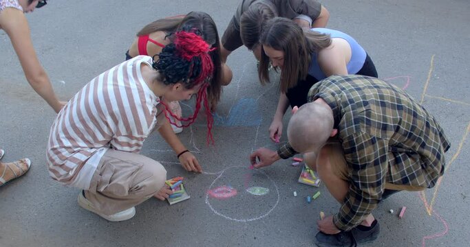 Young people start draw on asphalt with crayons. Group art therapy fosters social connection, provides opportunity to connect with peers who have similar experiences, reducing feelings of isolation.