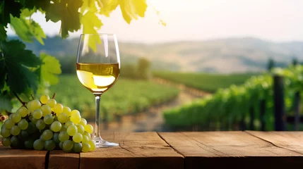 Foto op Canvas A glass of wine and a bunch of grapes, backdrop of a landscape with vineyards. © Olga Gubskaya