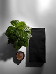 Black pouch template, top view, with a cup of brewed coffee, arabica tree, with shadows on the...
