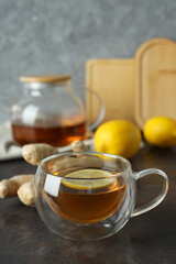 Cup and teapot with tea, lemon and ginger on gray background