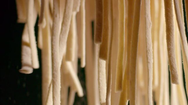 Flour is being thrown onto pasta noodles as they dangle in the air