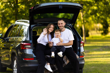 Young family three people sitting in car trunk before have picnic.