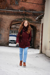 Fototapeta na wymiar Young redhead smiling girl with modern camera making photo in winter city