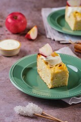 Sliced kugel, casserole of noodles, cottage cheese, apples and raisins on a green plate on a brown concrete background. Jewish cuisine. Noodle dishes.