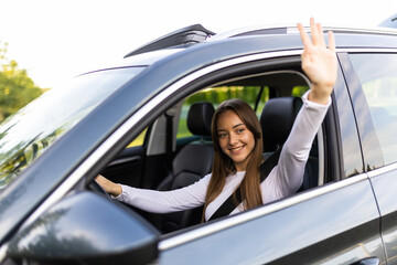 Young woman greeting with hand from car. Cheerful girl welcome somebody sitting in automobile