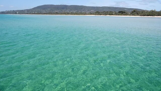 Background texture of beautiful shallow beach with white sand and clear turquoise sea water at Rosebud Beach, with mountains and trees in the distance. Mornington Peninsula VIC Australia.