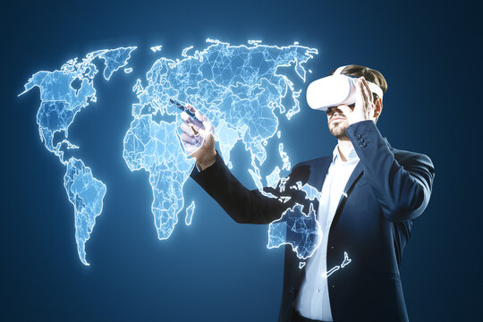 Attractive businessman with VR glasses using creative glowing polygonal map hologram on blurry blue background. Global community, virtual reality and network concept.