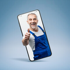 Cheerful repairman and plumber giving a thumbs up in a smartphone videocall and smiling, online  service concept