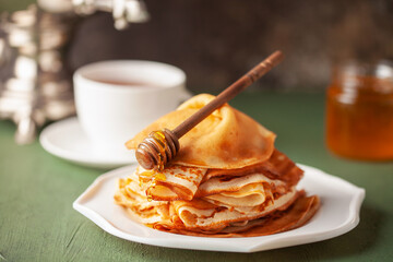 Pancakes or crepes in a plate with honey and tea