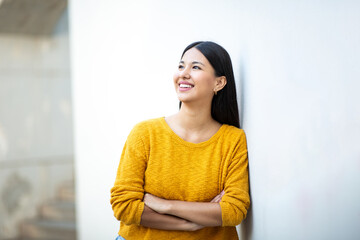 beautiful young smiling woman with arms crossed while leaning against wall