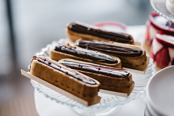 Eclairs sprinkled with chocolate cream. Candy bar on wedding feast closeup. Delicious reception luxury ceremony. Table with sweets, candies, and dessert. Culinary and cooking concepts.