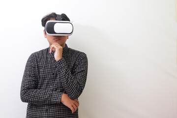 Portrait of Asian man in black plaid shirt using Virtual Reality (VR) glasses and thinking with hand on chin. Isolated image on white background
