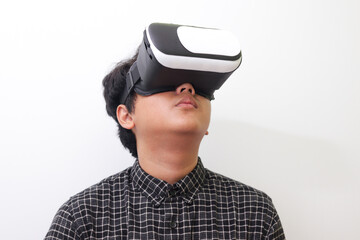 Portrait of Asian man in black plaid shirt using Virtual Reality (VR) glasses and looking up....