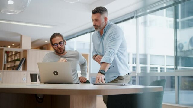 Tech professionals working together to create solutions for their software design project. Business men using a laptop as they discuss ideas for innovative web development.
