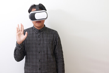 Portrait of Asian man in black plaid shirt using Virtual Reality (VR) glasses and greet his friend inside the game with opened palm. Isolated image on white background