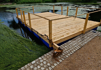 Pier for park visitors. two steps lead to it. planks terrace over water. Pond with a dock for...