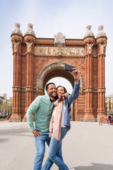 Beautiful happy hispanic latino couple of lovers dating outdoors - Tourists in Barcelona having fun during summer vacation and visiting Arc de Triumf historic landmark - obrazy, fototapety, plakaty