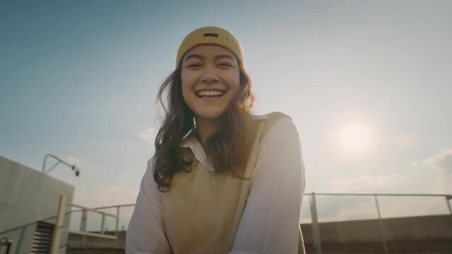 Young Gen Z girl asia people curly brown hair, face, eye smile in blue sky sun light lens flare. Teen urban city life happy joy of future hope enjoy warm time relax sunset. Good mental health teenage.
