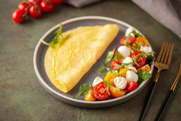 Salad with arugula, mozzarella and tomatoes in a plate on the table. Omelette with Caprese salad.