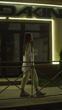 girl walking on the sidewalk along the street in the evening, vertical video