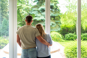 A couple standing at the window at home and looking out