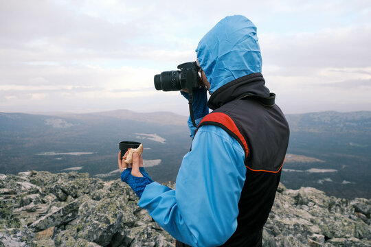  photographer with tea and a sandwich in his hand on top of a mountain takes pictures of the landscape.Active lifestyle
