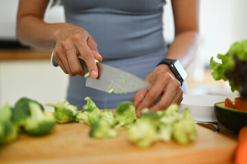 Cropped shot of woman cutting fresh broccoli, preparing healthy meal in kitchen. Healthy lifestyle concept