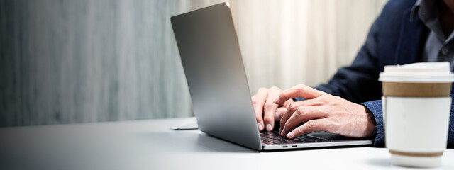 Panorama closeup of businessman hands typing writing and using laptop desktop keyboard while...