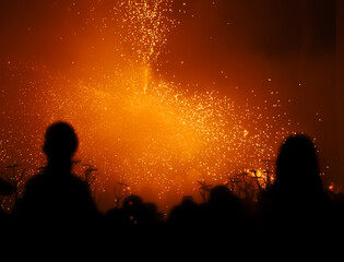 Silhouettes of people and a child on his father's shoulders watching the pyrotechnic show of the devils and Correfocs on a street in Granollers at night during the traditional festival.