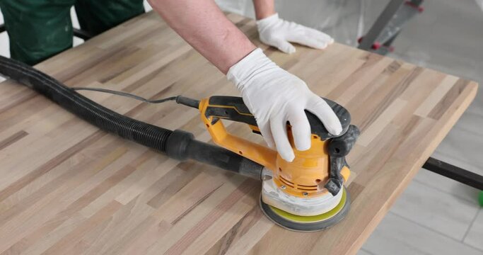 Carpenter polishes wood with wood workshop sanding machine. Master sands and polishes wood surface