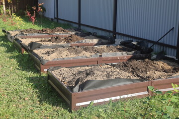 Beds with soil in a vegetable garden on a sunny day. Filling the beds with humus in the fall, metal beds.