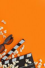 Popcorn, 3d glasses and clapperboard on a orange background. Flat lay, copy space