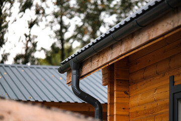 Dark plastic drainage system of a private house. Drainage system under the roof of a wooden house