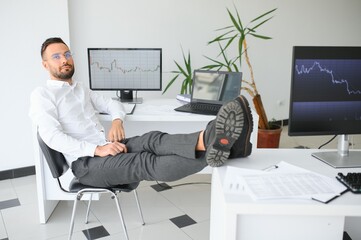 Young businessman is relaxing at workplace and has his feet on desk in office.