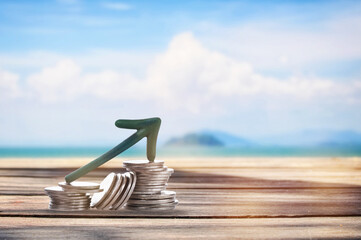 Stack of coins with arrow upwards on planks on tropical beach background. Business beginning with...
