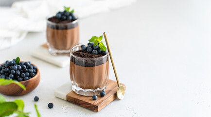 Healthy vegan chocolate mousse with fresh blueberry and mint in glasses on white background. Homemade Chocolate mousse from aquafaba. Chocolate vegan pudding recipe. Protein diet. Copy space