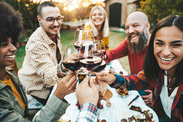 People clinking red wine glasses on garden dinner party - Happy friends eating meat and drinking...